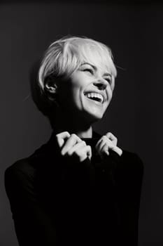 Smiling woman with short blonde hair showing happiness and confidence while wearing a black top. Set against a dark background, this image conveys joy and positivity.