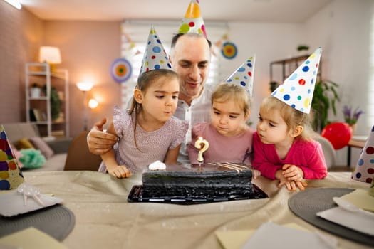 Children gather around a cake, ready to make a wish and blow out candles.