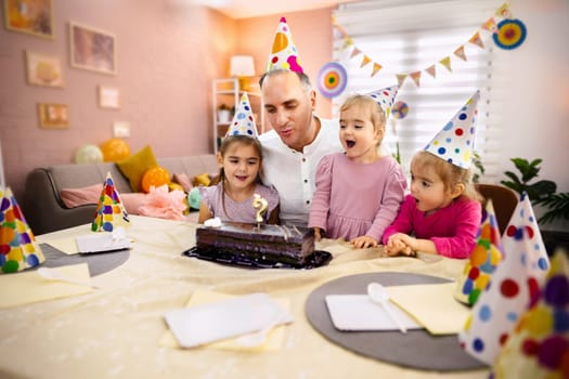 Family gathers around a chocolate cake as children cheer in excitement.