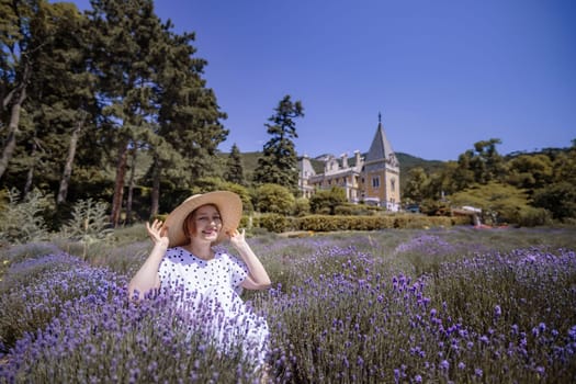 A woman is sitting in a field of purple flowers. She is wearing a straw hat and a white dress. The field is full of lavender, and the sky is clear and blue. The scene is peaceful and serene