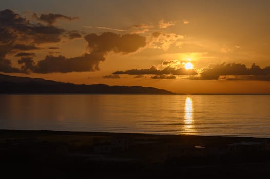 As the day comes to a close, a brilliant sunset lights up the horizon, painting the sky with warm hues. Gentle waves lap at the shore, creating a peaceful atmosphere by the water.