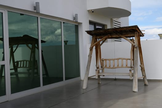 A rustic wooden swing hangs invitingly on a sleek terrace, reflecting the contemporary design of the building. Clear skies provide a serene atmosphere for peaceful moments outdoors.
