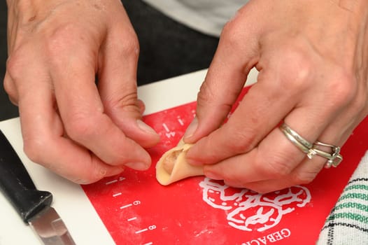 Hands skillfully fold dumplings on a vibrant red board, reflecting the joy of culinary creation on a sunny afternoon, adding warmth to the gathering of friends.