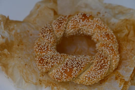 Delight in the warm, inviting aroma of freshly baked sesame bread, showcasing a braided shape on soft, crumpled paper, perfect for sharing during a relaxed afternoon gathering.