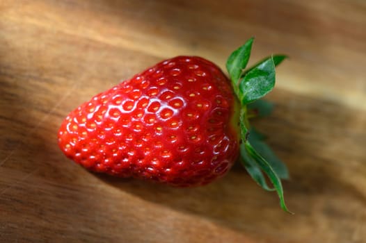 Juicy strawberry lies on a rustic wooden table, its shiny skin glistening in the sunlight, symbolizing freshness and summer's bounty, perfect for desserts or healthy snacks.