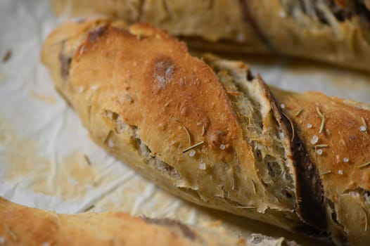 Golden brown artisan bread rests on a parchment-lined surface, showcasing a crispy crust sprinkled with sea salt and aromatic herbs, inviting taste and warmth to the senses.