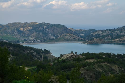A serene lake glistens under a soft sunset, surrounded by lush hills and gentle slopes. Nature thrives in this remote valley, offering a peaceful retreat for contemplation and relaxation.