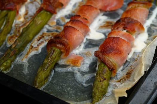 Asparagus stalks are wrapped in crisp pancetta, perfectly roasted to a golden brown on a baking tray. Aromas fill the air in a cozy kitchen as this enticing dish cooks.
