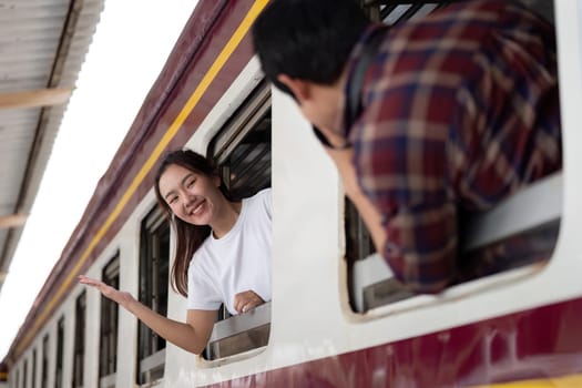 A couple enjoys their train journey, with one playfully waving from the window while the other captures the moment, highlighting their joyful adventure.