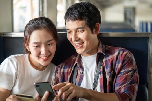 Inside the train, a couple shares laughter as they explore travel options on their smartphone, surrounded by a cozy environment, capturing their adventure.