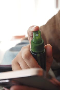 A person holds a mist spray bottle while using a smartphone nearby.