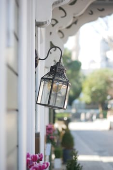 A stylish street lamp hangs beside a vibrant flower display on a sunny day.