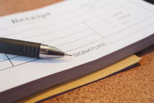 A pen rests on a receipt ready for signature on a wooden surface.