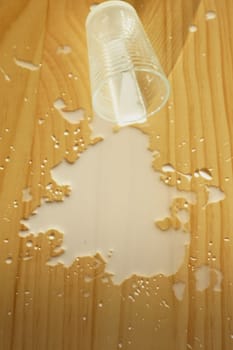 milk spilled on wooden surface with a plastic cup resting nearby.