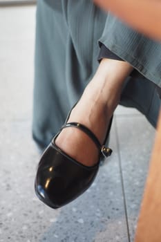 A person in a long skirt sits, showcasing a black strap shoe on their foot.
