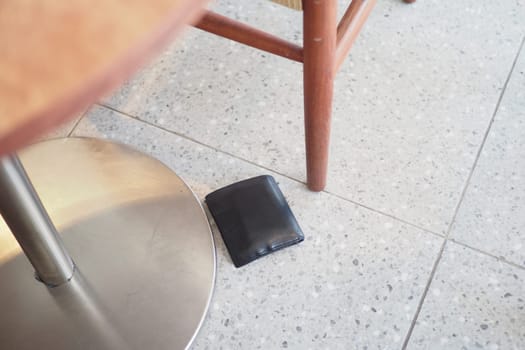 A black wallet lies on the floor beside a wooden table.