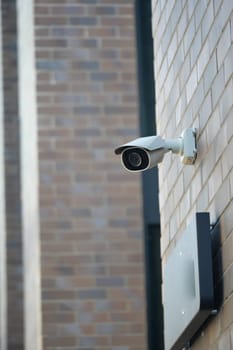 A security camera is positioned high on a brick wall watching the entrance.