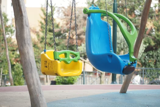 Two swings in bright colors hanging from sturdy chains in a park setting.