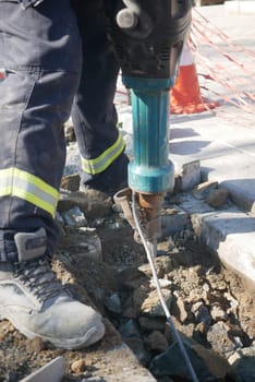Worker operates a jackhammer breaking concrete during road repairs.