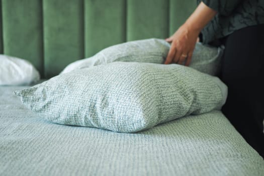 Someone adjusts two soft pillows on a well-made bed in a calming space.