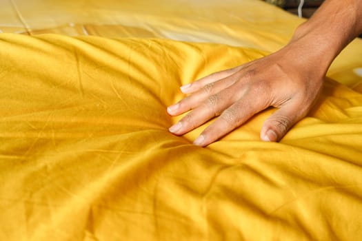 A hand presses down on a vibrant yellow pillow, creating a soft impression.