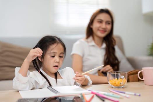 In a cozy setup, a young girl enthusiastically draws as her mother enjoys the moment, emphasizing a supportive learning environment at home.