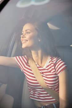 A cheerful young woman enjoys a ride in a car, looking out the window with a bright smile