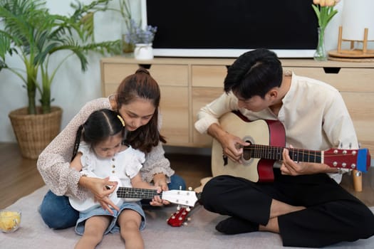 A tender family scene where a mother helps her daughter strum a ukulele, showcasing parenting, love, and musical engagement.