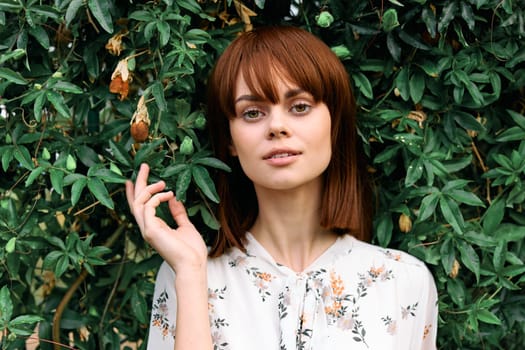 Vibrant redhead woman posing in front of lush green bush with leaves