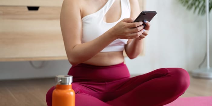 A wellness enthusiast takes a moment to hydrate and connect with her phone after enjoying a calming yoga routine, exemplifying self-care.