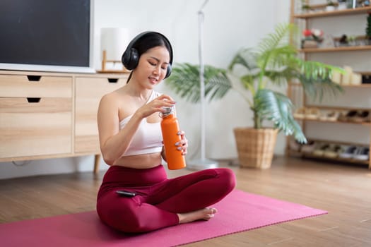 A woman takes a moment to hydrate with an orange bottle, enhancing her wellness practice and ensuring she stays energized during her yoga session at home.