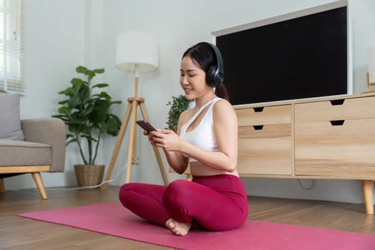 Sitting comfortably on a yoga mat, a woman enjoys her favorite playlist of mindfulness music on her phone, promoting relaxation and wellness in her cozy home environment.