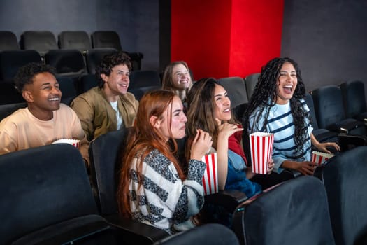 Group of young people enjoying a movie at the cinema, sharing laughter and smiles while munching on popcorn and having a great time
