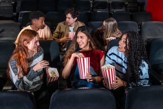 Cheerful multi ethnic friends enjoying popcorn while watching a film together in a cozy movie theater, sharing laughs and smiles