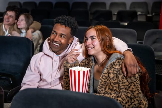 Happy couple sharing popcorn while watching a movie at the cinema, enjoying a night out with friends