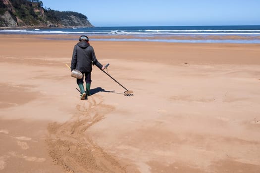 Man with metal detector walking on sandy beach searching for treasures.