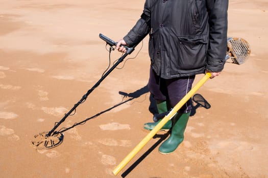 Male adult searching beach for treasures with metal detector and sand scoop.
