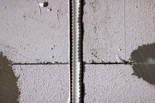A close up view of a weathered concrete wall featuring a thin wire running through its solid structure and material