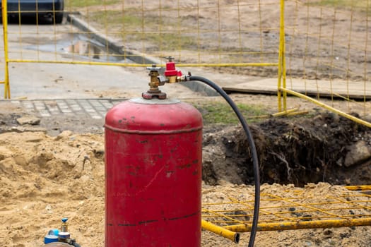 A vibrant red gas cylinder, complete with a hose connected to it, is located in the dirt. This setup may potentially be related to various applications