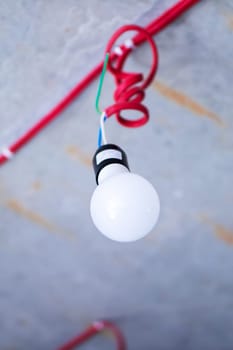 A bright and shiny light bulb is hanging down from a vibrant red cord that adds a pop of color to the scene