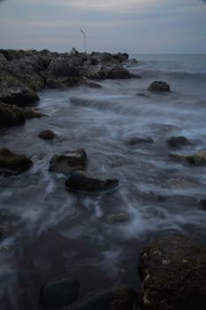 As twilight descends, gentle waves swirl around the rugged stones along the shore, creating a serene atmosphere that invites tranquility and reflection by the water's edge.