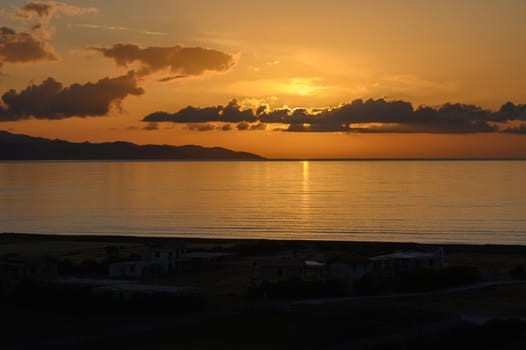 Golden sunlight reflects on calm waters as the sun descends behind distant hills, creating a peaceful twilight atmosphere along the tranquil coastline. The beauty of nature inspires serenity.