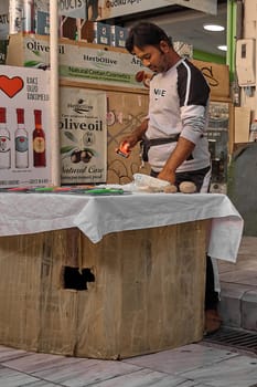Crete, Greece - April 5, 2025: At a vibrant outdoor market, a merchant demonstrates a kitchen gadget surrounded by fresh produce and advertising posters.