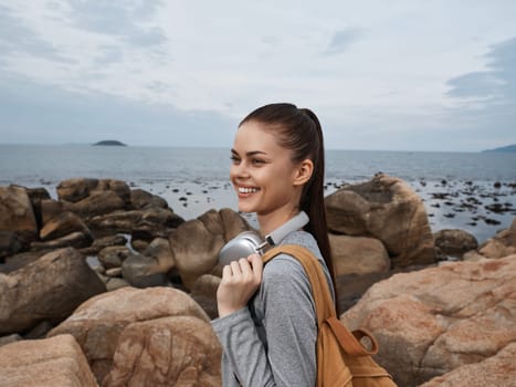 Joyful woman enjoying nature by the ocean, carrying reusable water bottle and wearing casual athletic clothing, embodying healthy and active lifestyle
