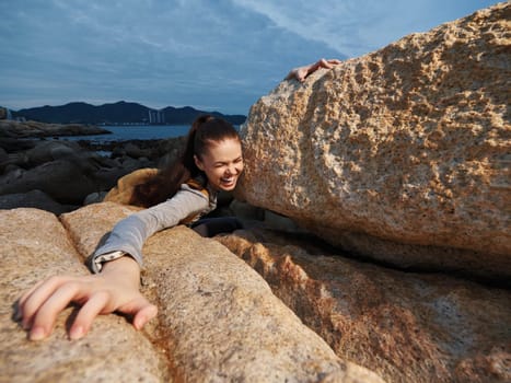 A joyful young woman is playfully caught between large rocks at the beach, radiating a sense of adventure and freedom with a stunning coastal view