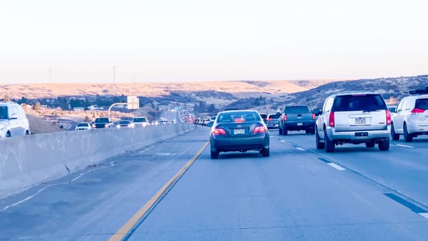 Denver, Colorado, USA-January 26, 2024-Vehicles are lined up during the morning rush-hour on a highway leading from suburban areas towards Denver, with the golden hues of sunrise illuminating the scene.