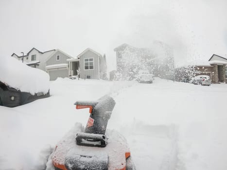 Denver, Colorado, USA-February 4, 2024-View from a snow-blanketed driveway captures a residential area mid-snowfall, with houses partially obscured by the cascading white flakes and a snow-covered car in the foreground.