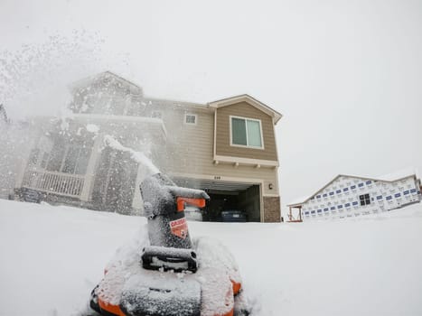 Denver, Colorado, USA-February 4, 2024-View from a snow-blanketed driveway captures a residential area mid-snowfall, with houses partially obscured by the cascading white flakes and a snow-covered car in the foreground.