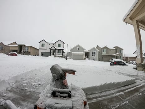 Denver, Colorado, USA-February 4, 2024-View from a snow-blanketed driveway captures a residential area mid-snowfall, with houses partially obscured by the cascading white flakes and a snow-covered car in the foreground.