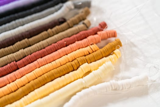 A vibrant collection of clay beads, neatly arranged by color on a white table, ready to inspire young crafters to create their own unique bracelets.